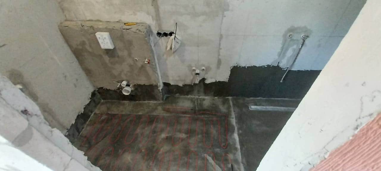 Hidroizolație aplicată pe pardoseală și pereți, cu cablu de încălzire în pardoseală montat pe plasă și rigolă liniară.