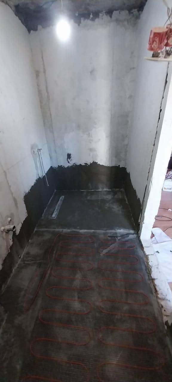 Zonă umedă pregătită: hidroizolație continuă pe pardoseală și pe partea de jos a pereților, cu rigolă liniară montată la pantă.