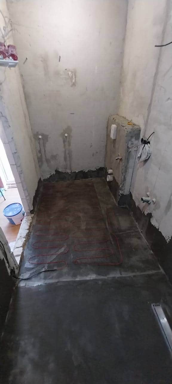 Cablu de încălzire în pardoseală fixat pe plasă peste hidroizolație, înainte de turnarea șapei.