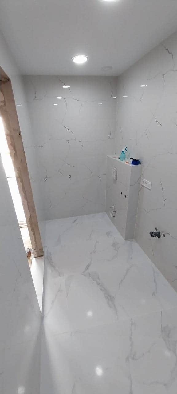 Baie finalizată în plăci albe aspect marmură, lucioase, cu zonă de duș fără prag și coloană pentru rezervor încastrat.