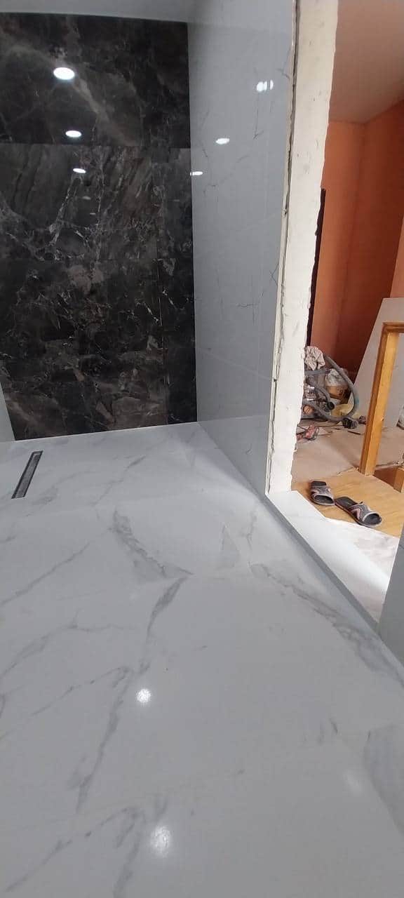 Perete de accent din plăci aspect marmură neagră, în contrast cu placarea albă și rigola liniară din pardoseală.