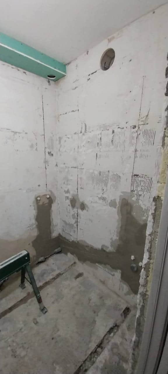 Pereți de baie curățați până la suport, cu urme de adeziv pieptănat și zone de mortar reparate înainte de placare.