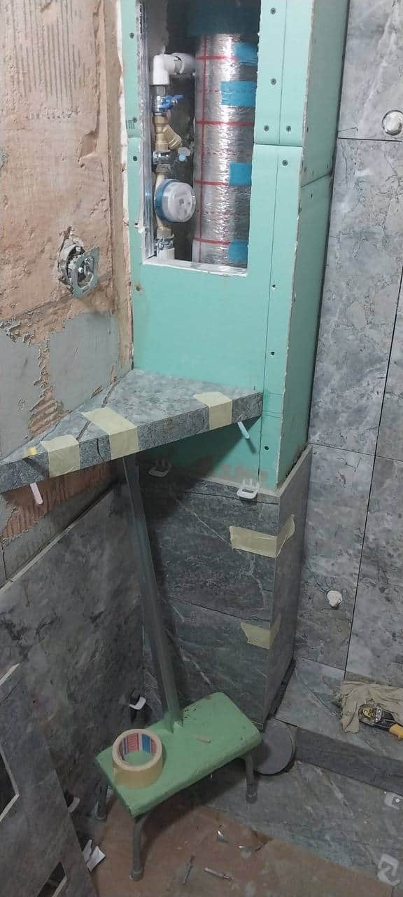 Nișă tehnică lăsată deschisă pentru apometru și tubulatura de ventilație, cu poliță placată și fixată cu bandă.