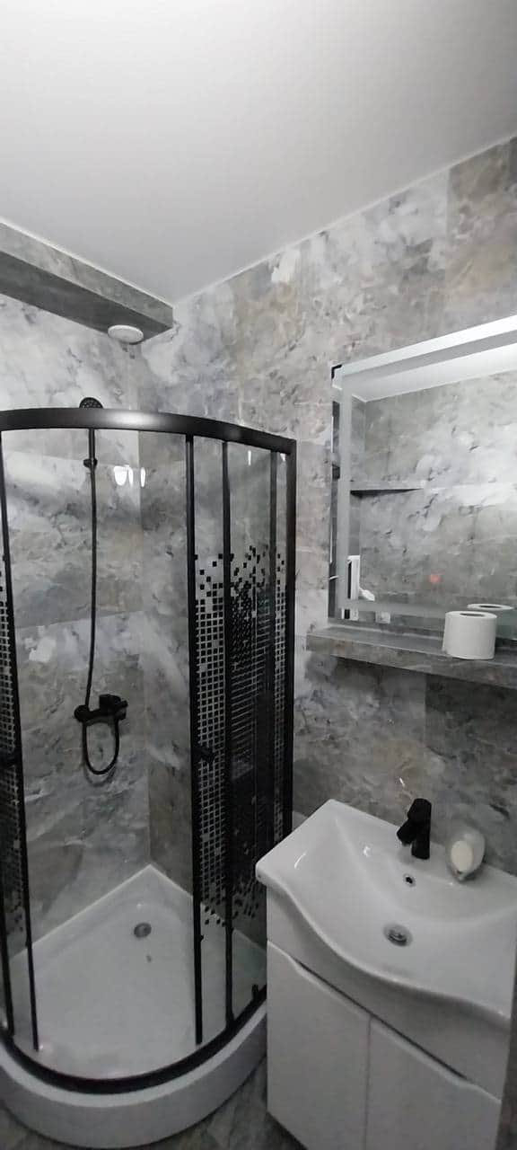 Vedere de ansamblu a băii finalizate: cabină de duș, lavoar cu mobilier alb și oglindă cu iluminare.