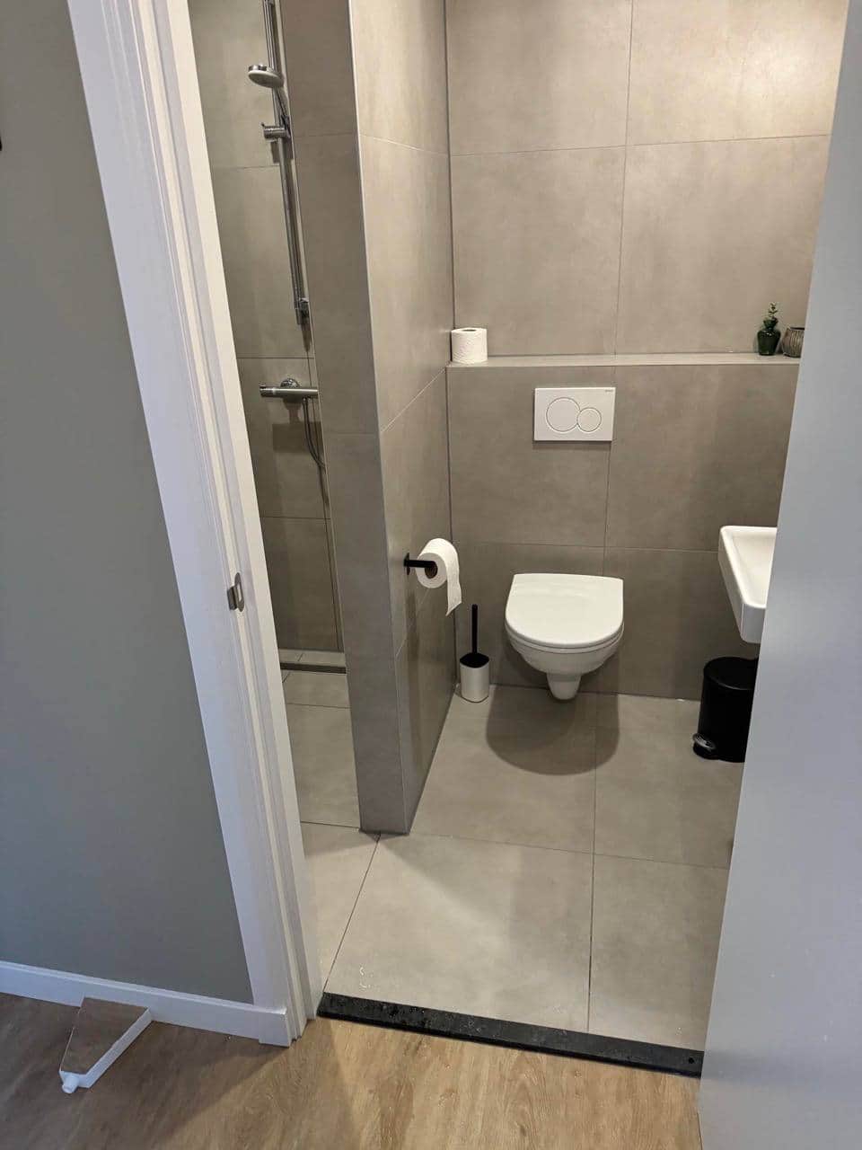 Baie compactă finalizată, cu plăci de format mare aspect beton, WC suspendat cu clapetă încastrată și nișă-poliță.